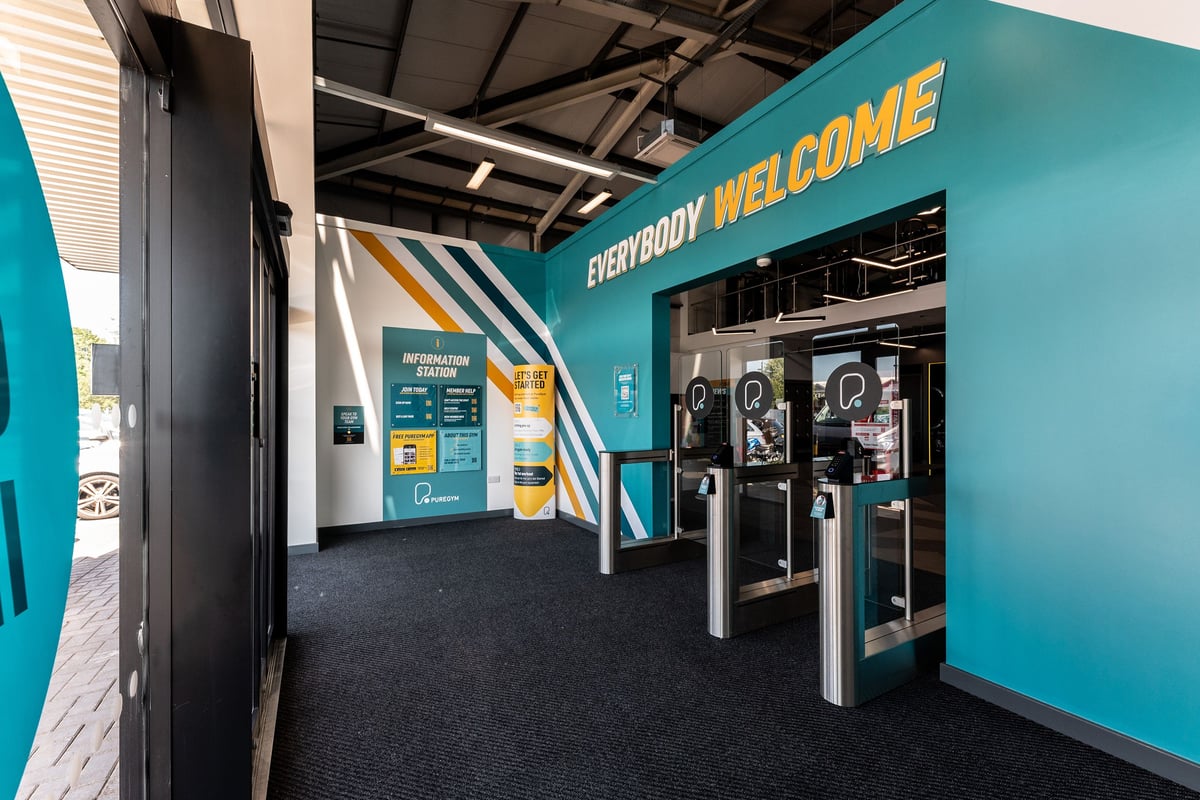 PureGym Crewe Grand Junction Retail Park: Turnstile entrance with self-service kiosks and digital displays.