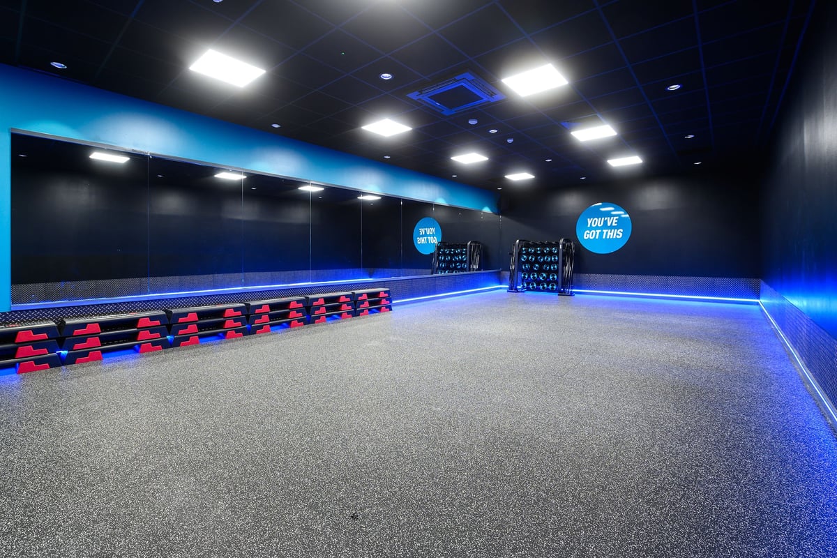 PureGym Bromsgrove Retail Park: Padded benches, rubberized flooring, and mirrored walls in a blue-lit studio.