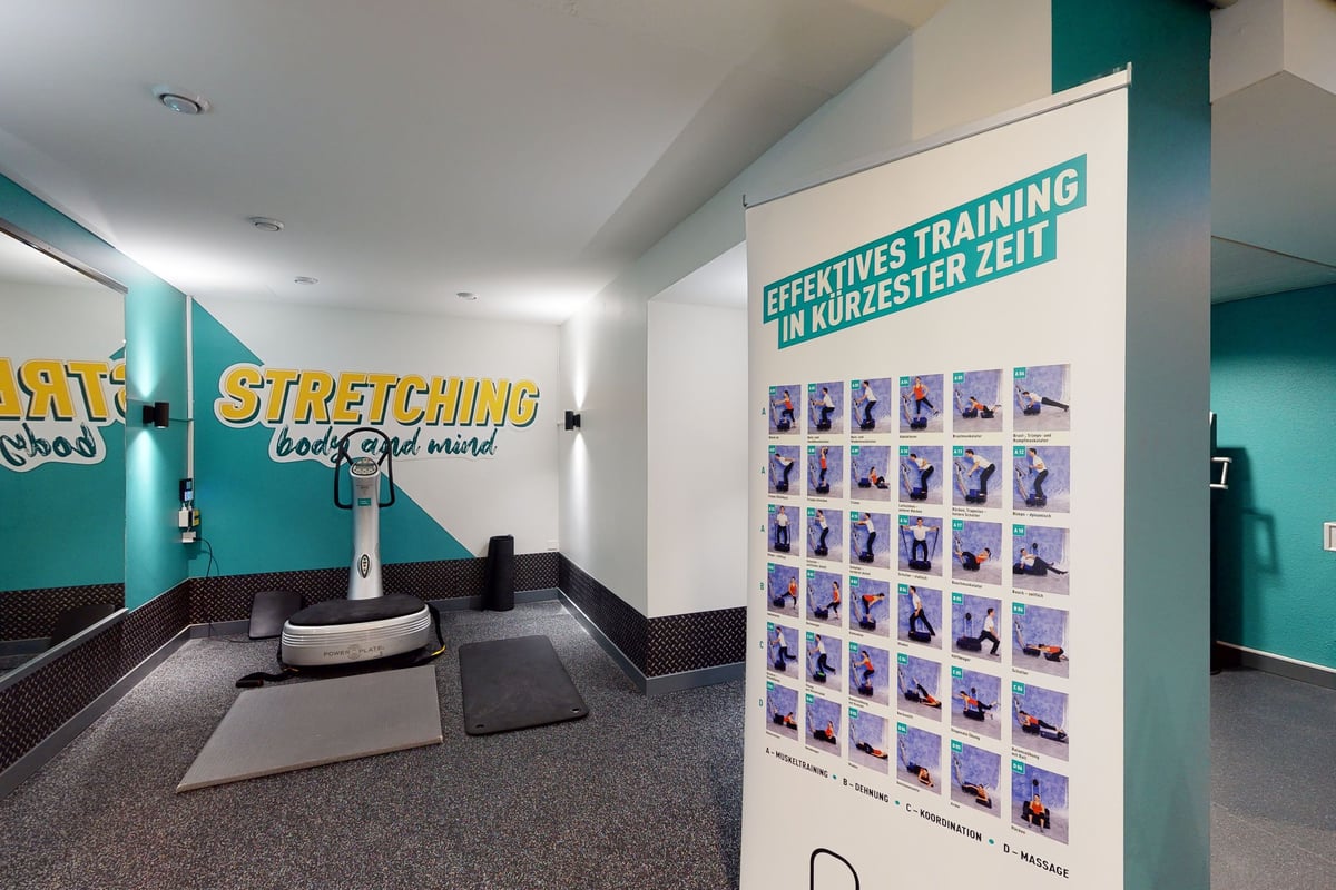 PureGym Bern Lorraine: Zone d'étirement avec tapis et rouleau, affiche présentant les étirements des exercices sous forme de grille.