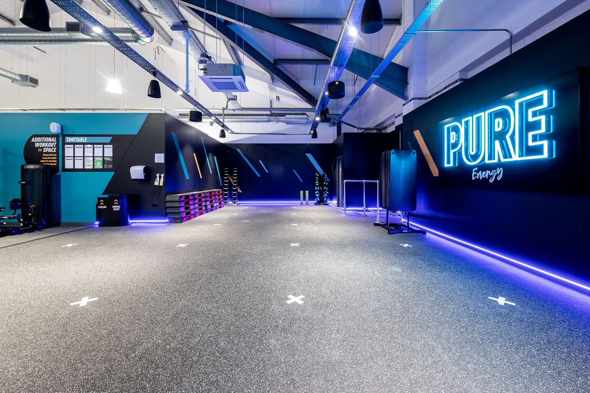 PureGym Stowmarket: Neon-lit studio space with rubberized flooring and branded signage along walls.