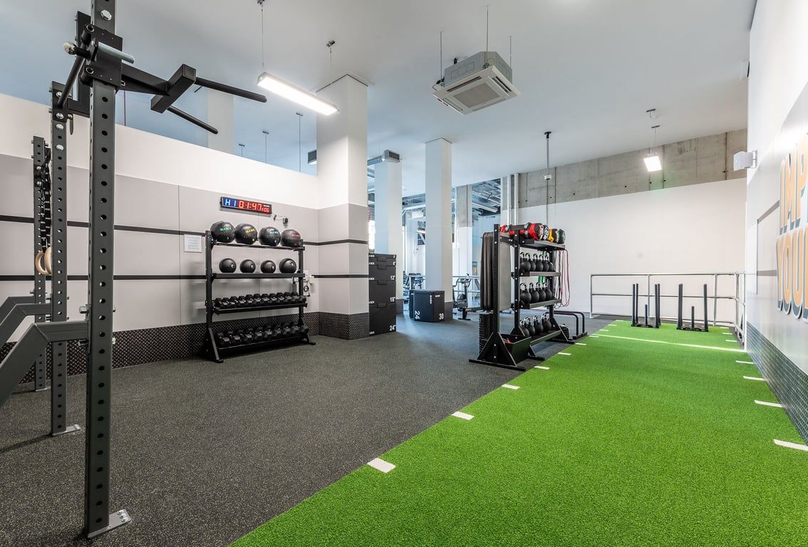 PureGym London Seven Sisters: Strength racks, weight plates, turf area, rubberized flooring in a bright gym studio.