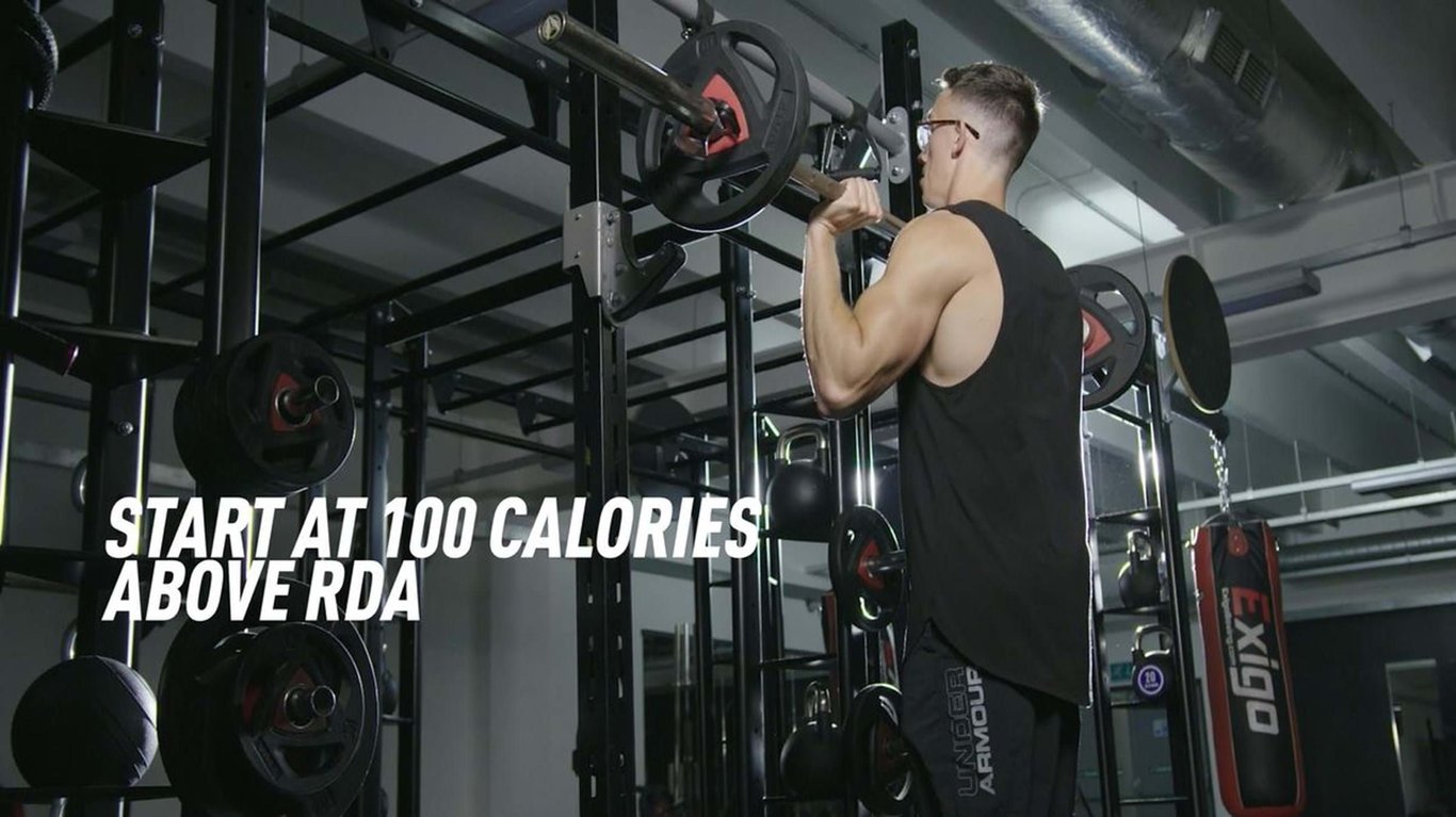 Man lifting barbell weights in gym with text start at 100 calories above RDA