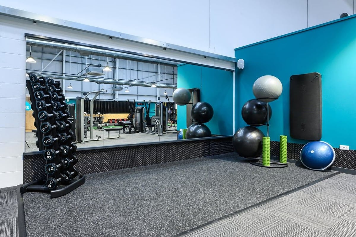 PureGym Saffron Walden: Racks of dumbbells, resistance bands, stability balls, rubberised floor, bright teal colour scheme.