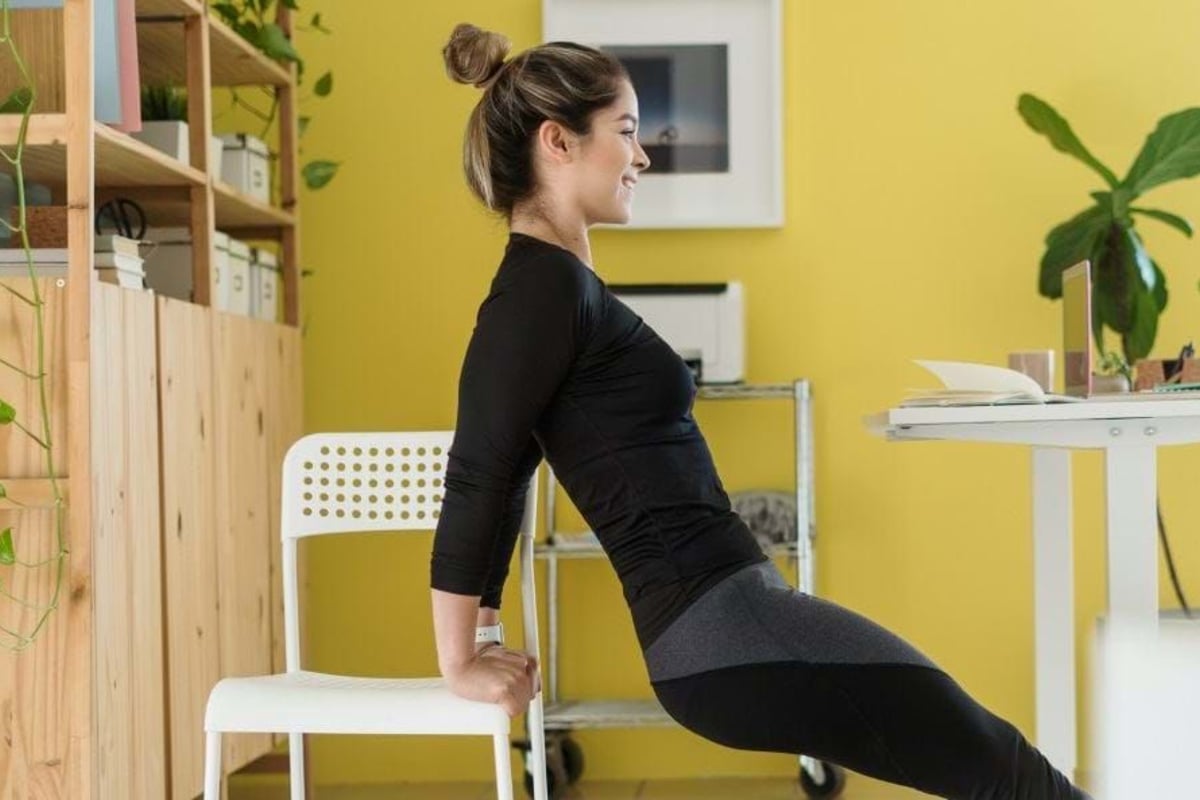 Woman exercising with chair in bright room with yellow wall and plants