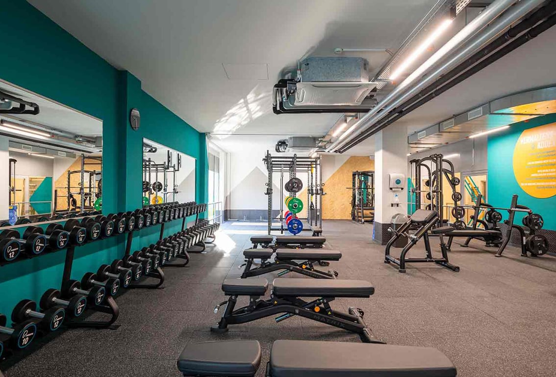 Puregym Brugg: Rows of weight benches, dumbbell racks, resistance machines in teal and gray colour scheme.