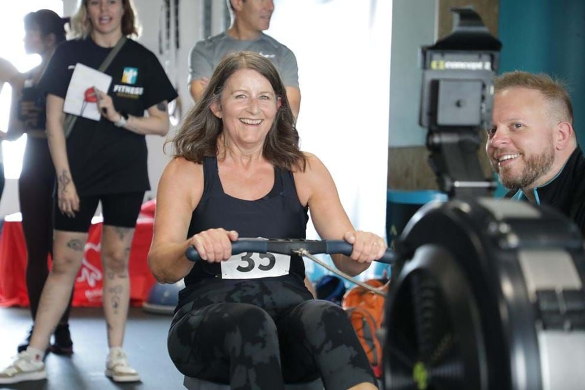 Woman smiling while using a rowing machine with people watching in the background