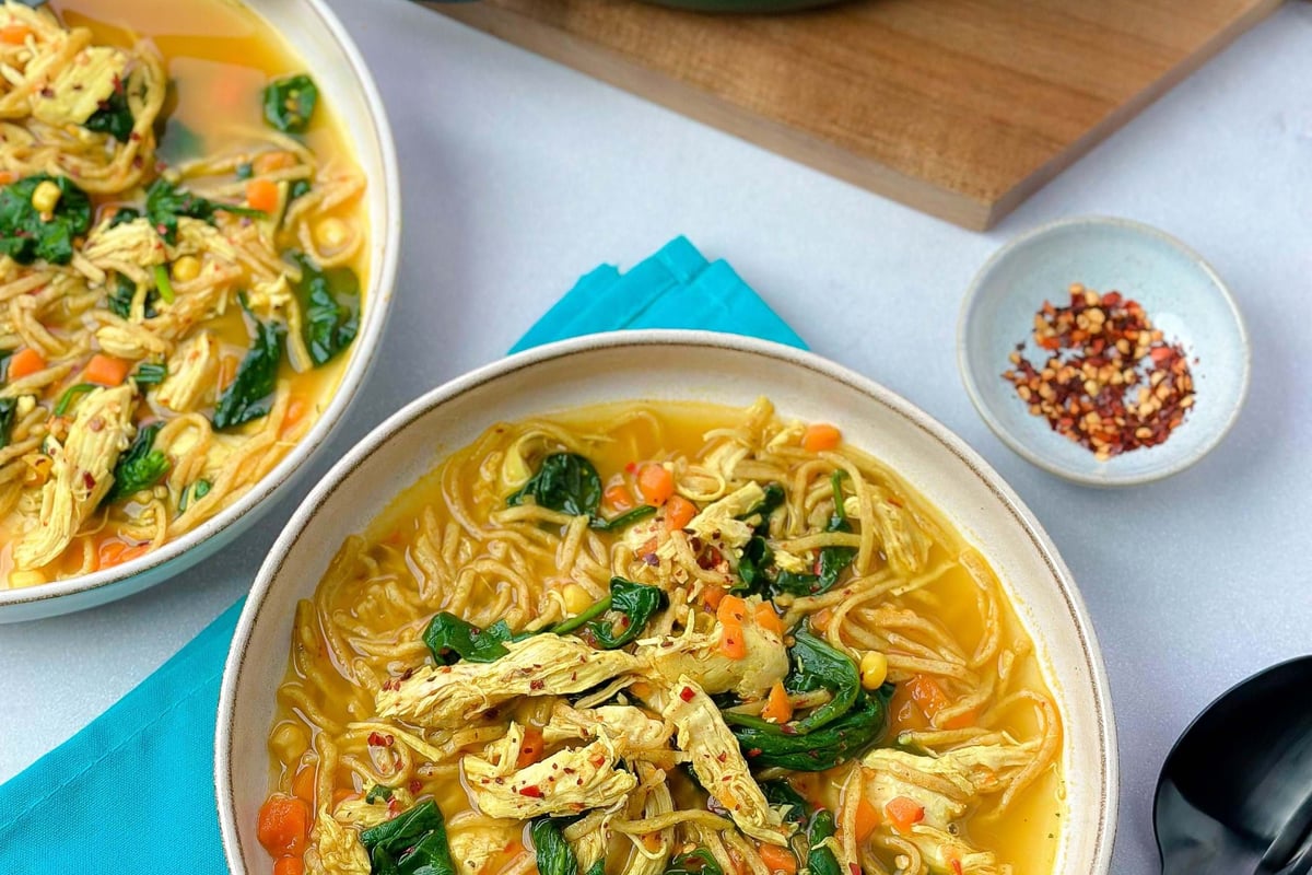 Bowls of chicken noodle soup with spinach and diced carrots on a table