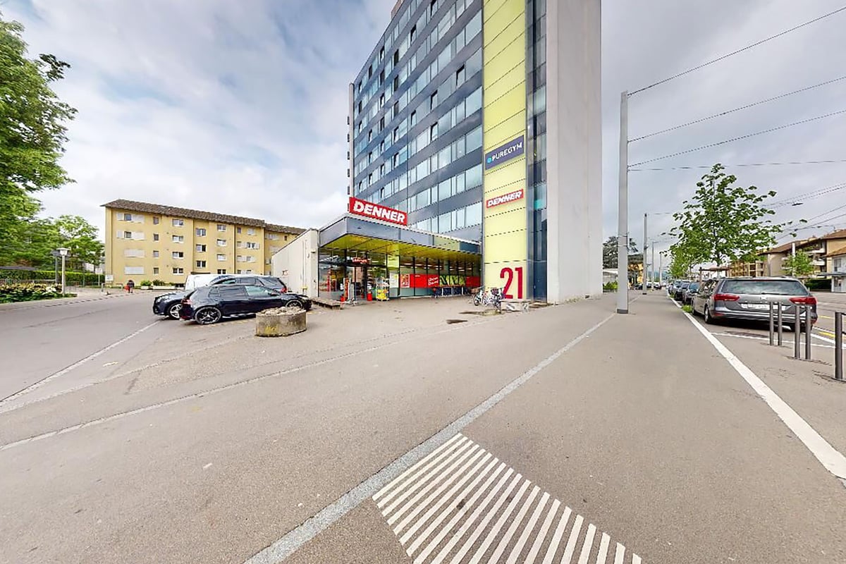PureGym Dietikon: Exterior view of urban road with parking, bicycles, and a multistory building with PUREGYM sign.