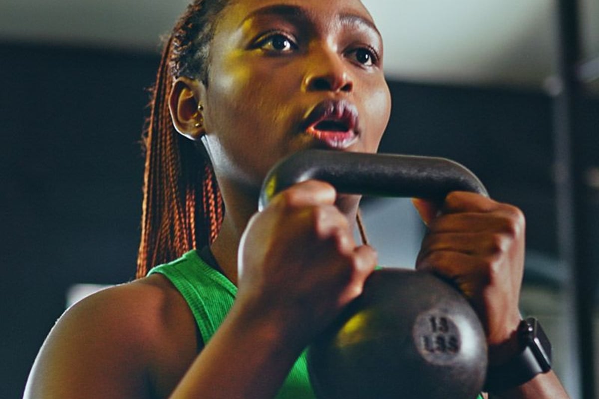 Femme en haut vert soulevant un kettlebell de 15 livres pendant l'entraînement