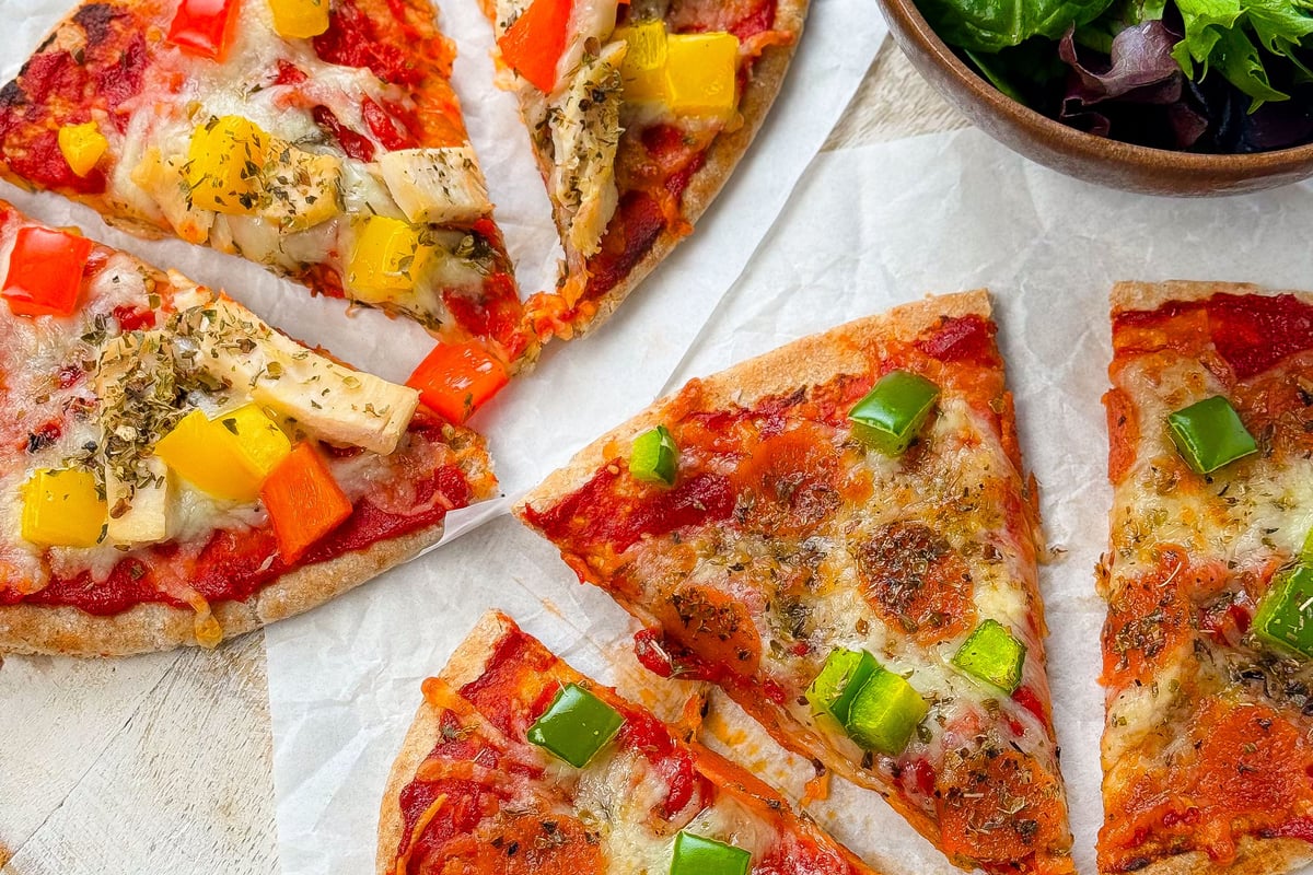 Slices of vegetable pizza with green salad in a wooden bowl on a round board