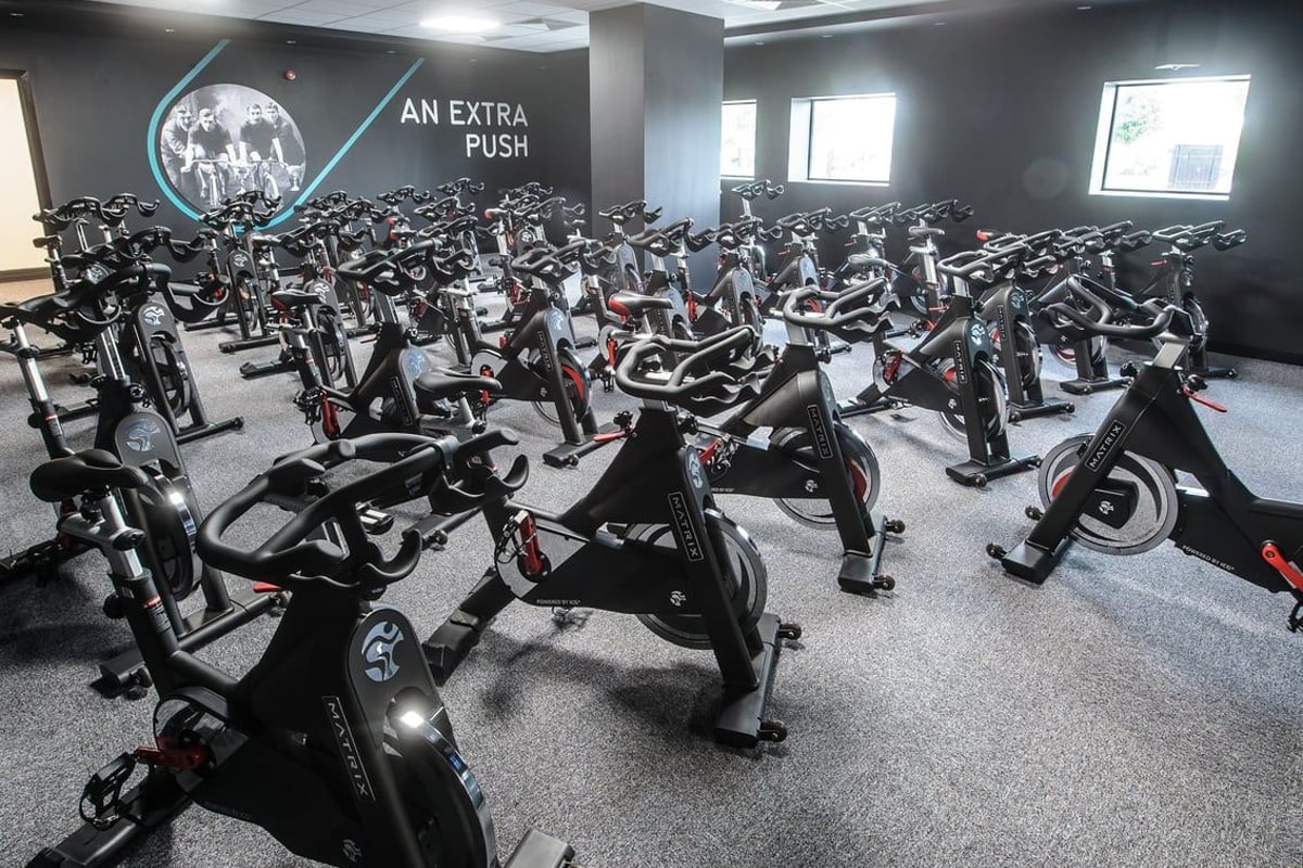 PureGym Denton: Rows of stationary cycles inside a dimly lit studio with motivational signage on the wall.