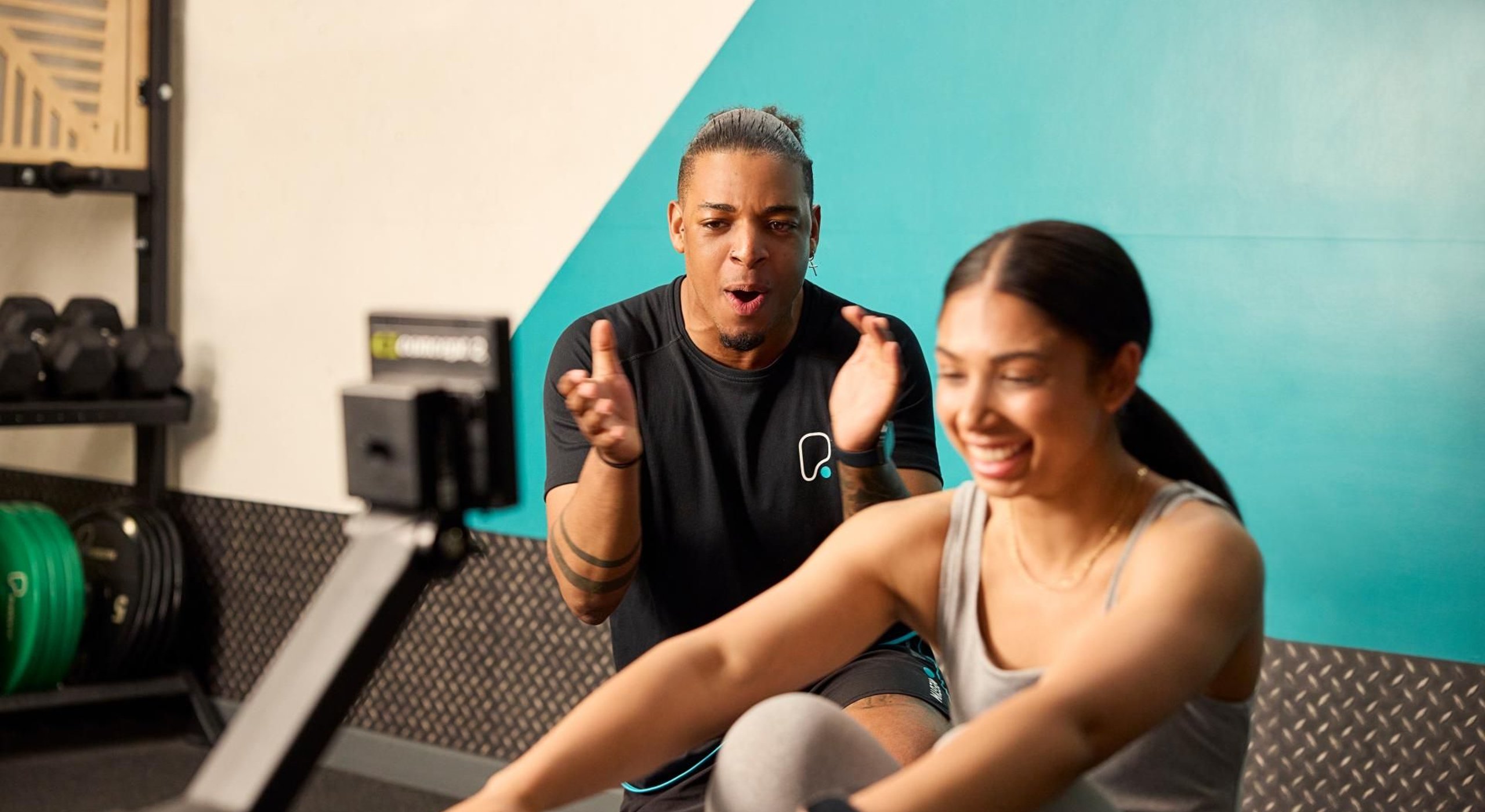A coach encourages a woman on a rowing machine in a PureGym