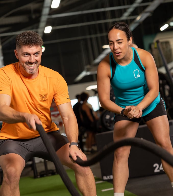 Feel PureGym Good: male gym user working with a battle rope assisted by female PT