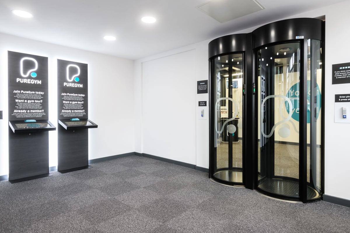 PureGym Brighton London Road: Revolving doors, signage for Puremotion gym brand, digital kiosks in small lobby area.