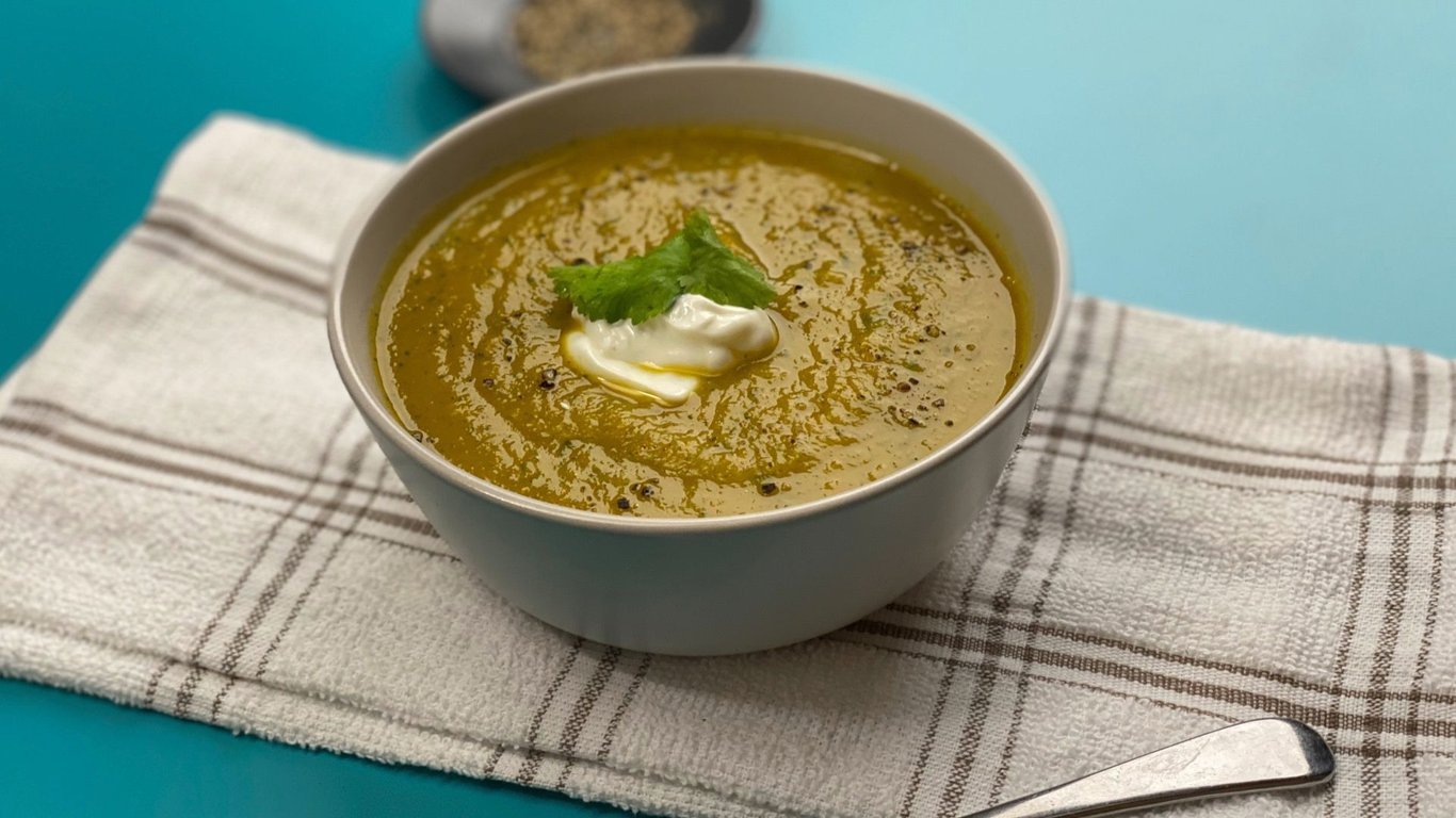 Bowl of green soup with cream and coriander leaf on a white checkered cloth