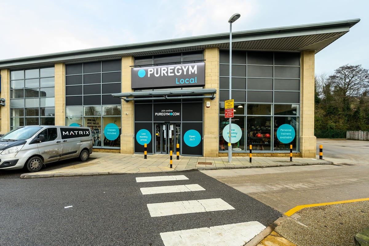 PureGym Glossop: Gym frontage with signage, parking spaces, and pedestrian crossing markings.