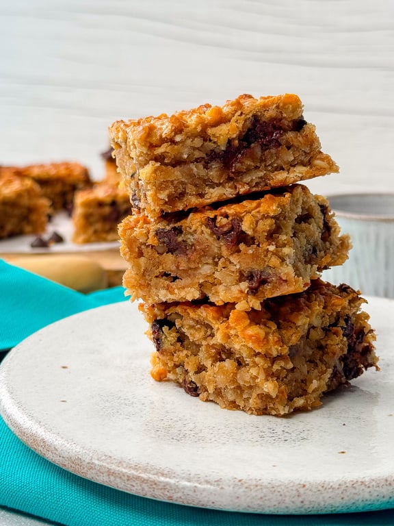 Stack of three chocolate chip oat bars on a white plate with a teal cloth underneath