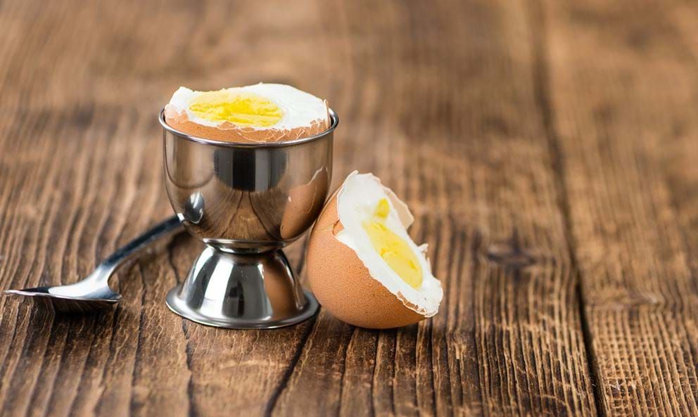 Soft boiled egg in a metal egg cup with a spoon on a wooden surface.