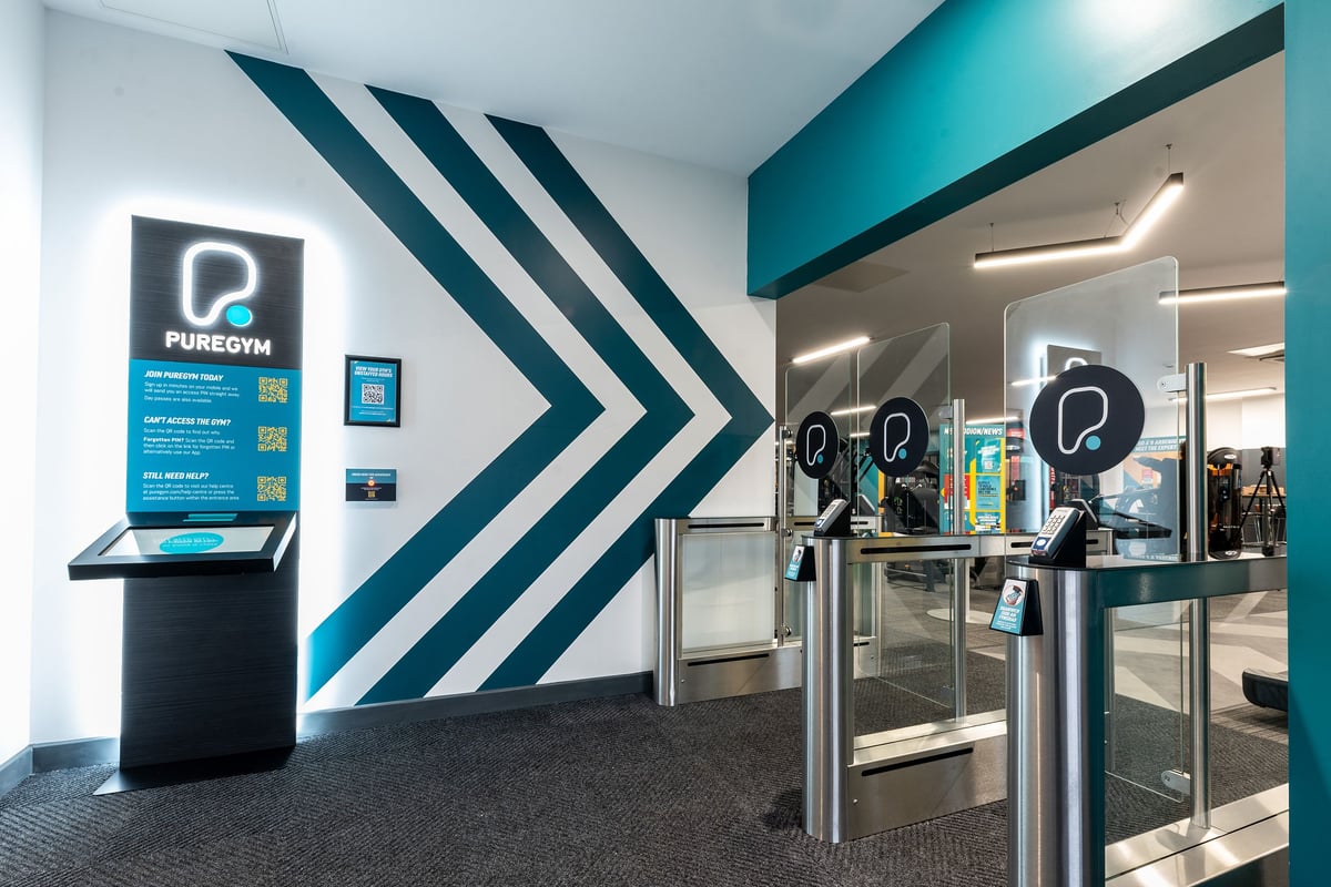 PureGym Bangor Wales: Turnstiles, signage for Puregym, and a sleek reception area with geometric teal wall designs.