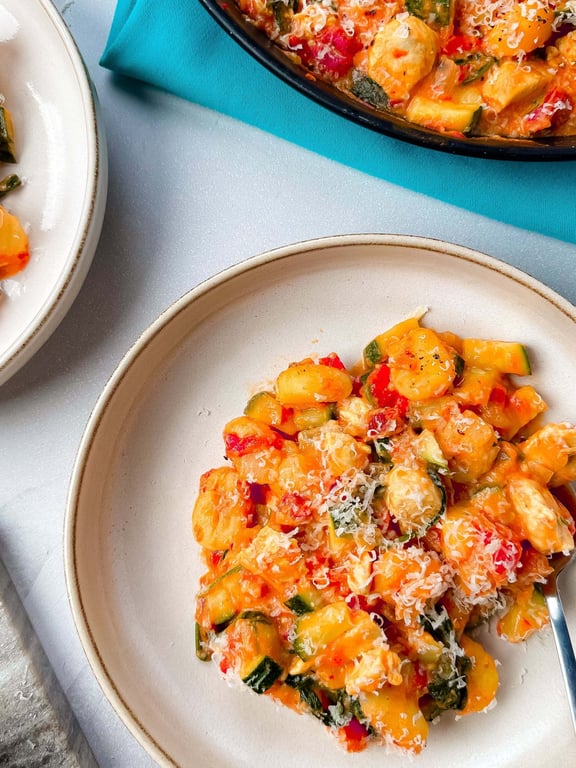Gnocchi with vegetables and grated cheese served on a beige plate with a fork.
