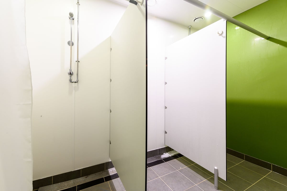 PureGym Bromborough: Shower stalls with green tiles and partition walls.
