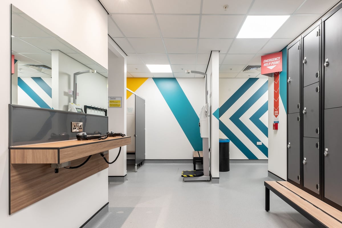 PureGym Nottingham Colwick: Reception area with wooden benches, lockers, and abstract geometric wall art.