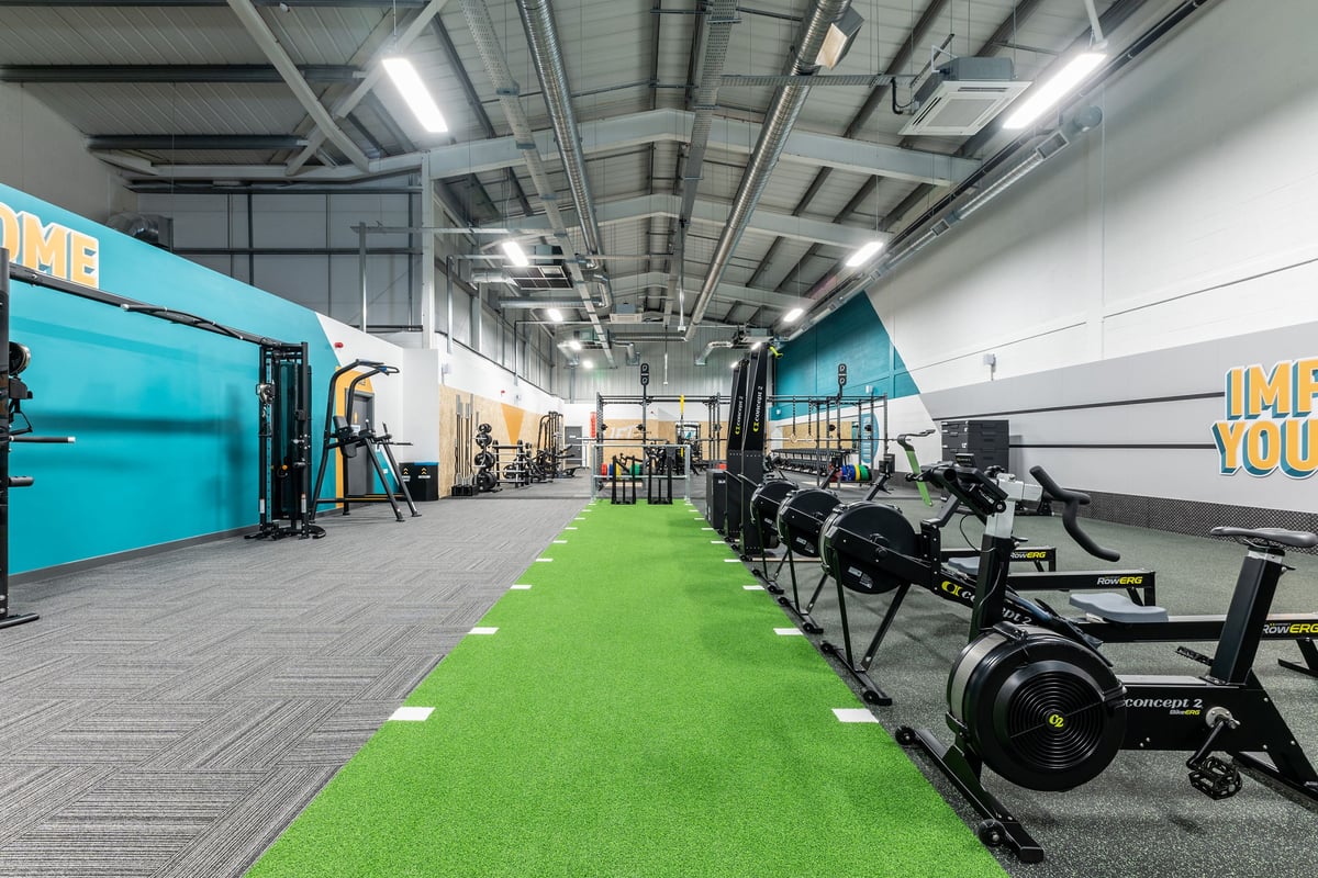 PureGym Byfleet: Rows of cardio machines, green turf area, free weights, and studio backdrop.