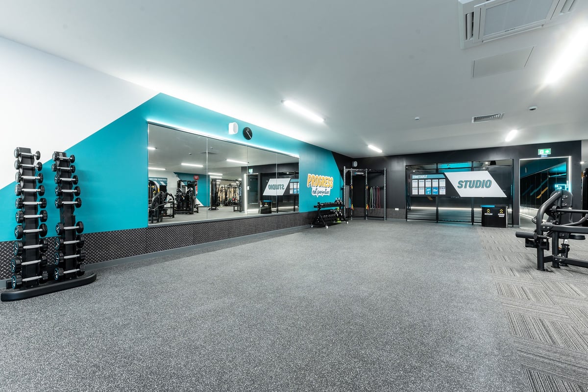PureGym Tyldesley: Teal-colored weight room with strength equipment, free weights, display monitors and rubberized flooring.