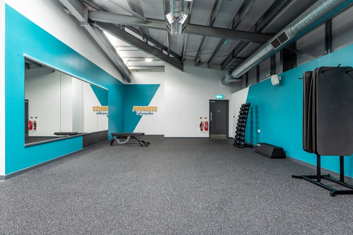 PureGym Coventry Warwickshire Shopping Park: Mirrored walls, resistance machines and free weights in a teal and grey gym.