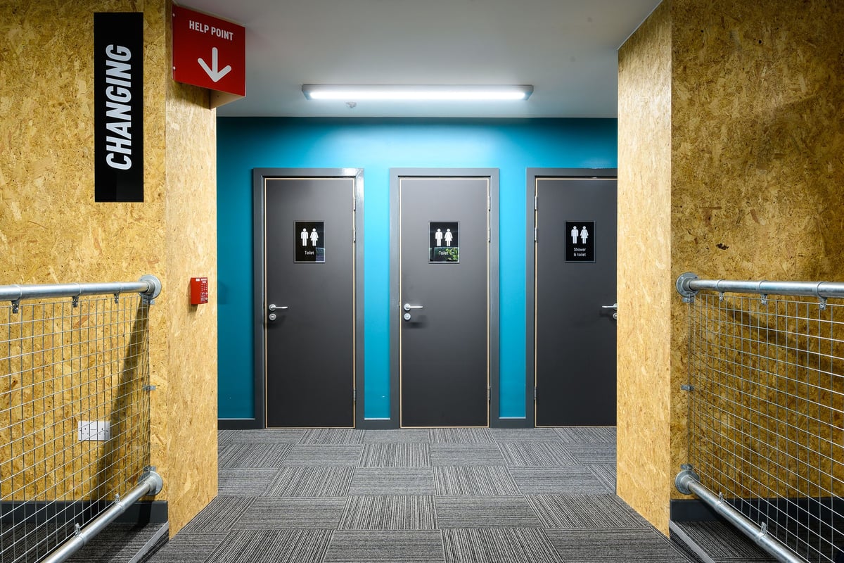 PureGym London Camberwell Southampton Way: Bathroom area with multiple closed stall doors and tile flooring.