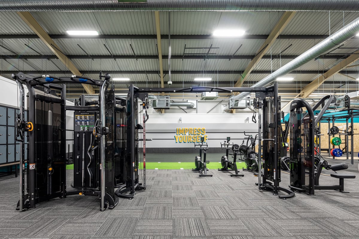 PureGym Neath: Rows of resistance machines, weight racks, benches, and rubberized flooring in a gym facility.