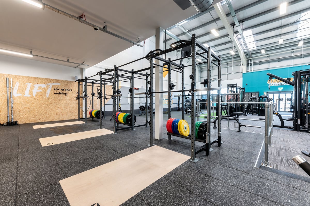PureGym Consett: Squat racks, weight plates, rubberized flooring, motivational wall art in a spacious gym area.