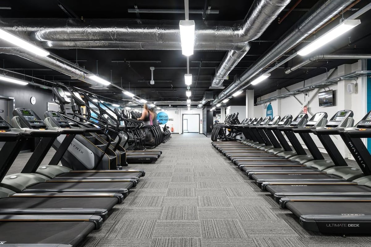 PureGym Glasgow Silverburn: Rows of treadmills, ellipticals, and other cardio machines in a dimly lit gym interior.