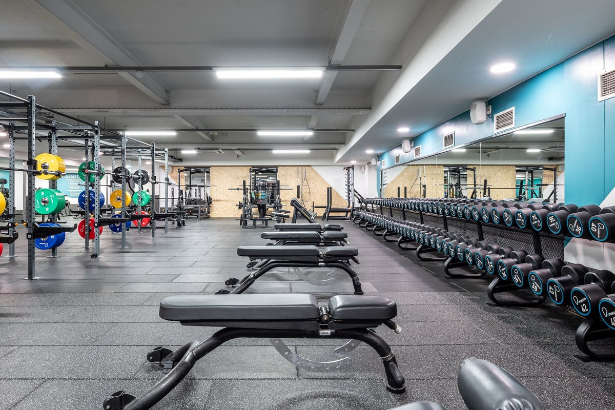PureGym London Marylebone: Weightlifting area with barbells, weight plates, benches, racks, and rubberized flooring.