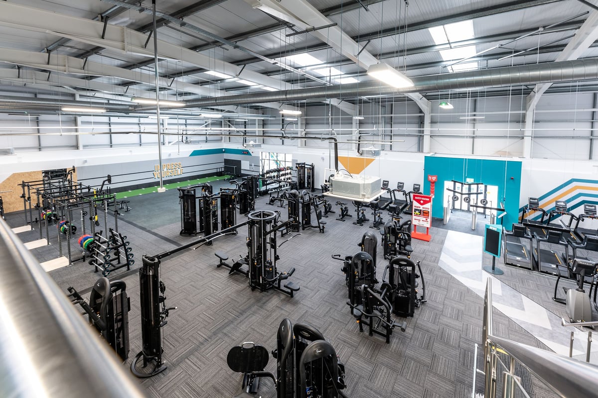 PureGym Blyth: Weight racks, benches, rubberised flooring, and signage in a spacious gym facility.
