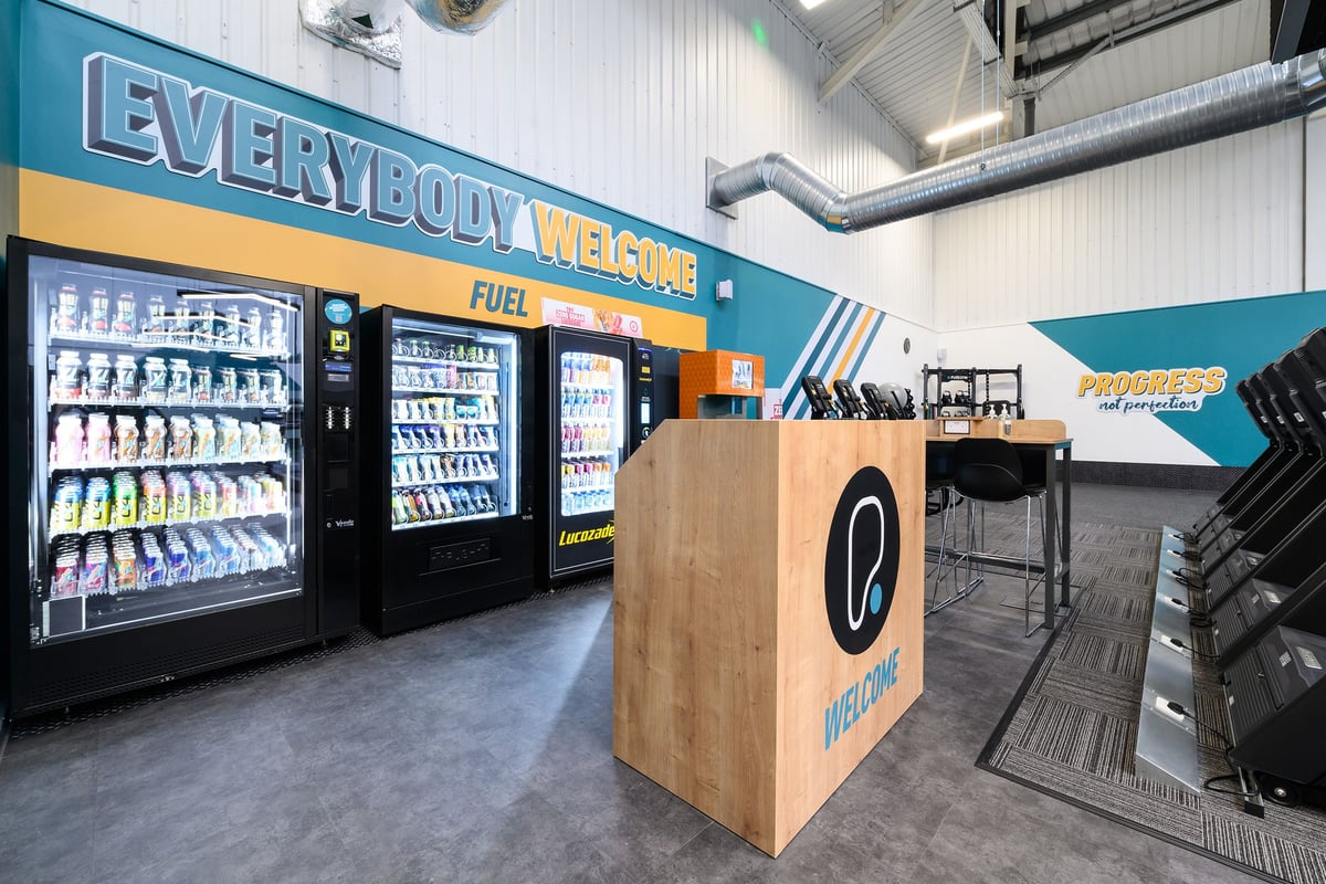 PureGym South Ruislip: Refrigerated vending machines, welcome counter, and fitness equipment in a brightly coloured space.