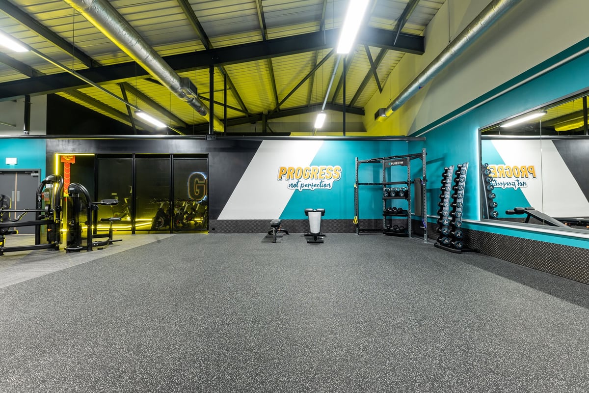 PureGym Ashton Under Lyne: Functional training area, weight racks, rubberized floors, teal accents, and mirrored walls.