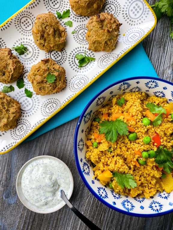 Falafel balls on a patterned tray with couscous salad and yoghurt dip on a wooden table