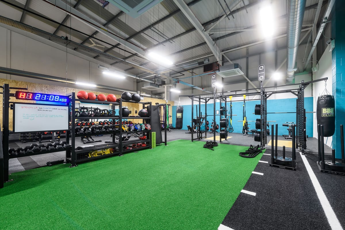 PureGym Buckingham: Gym with weightlifting racks, dumbbells, punching bags, turf area, weight plates, and digital timers.