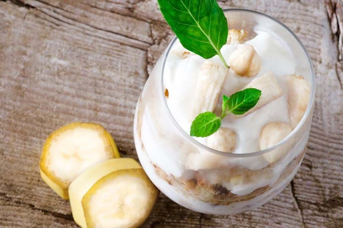 Banana slices and nuts in creamy dessert garnished with fresh mint leaves on wood
