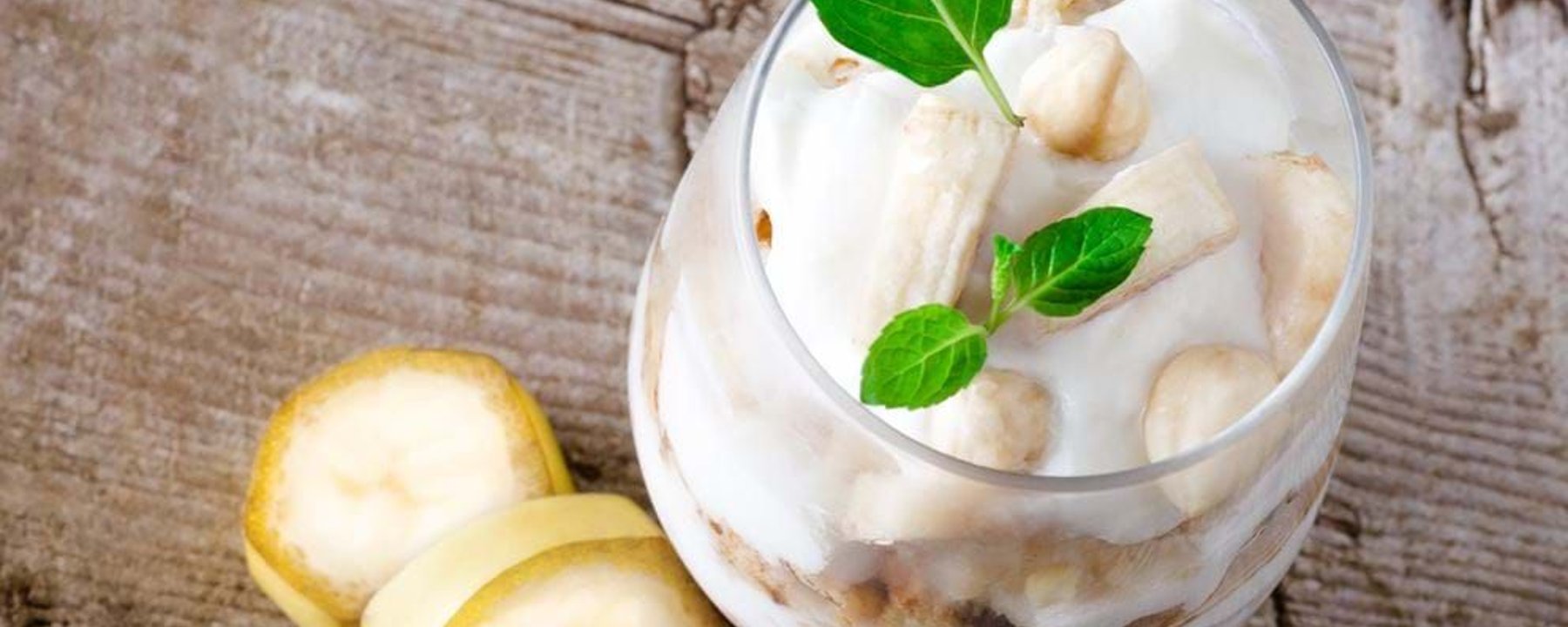 Banana slices and nuts in creamy dessert garnished with fresh mint leaves on wood