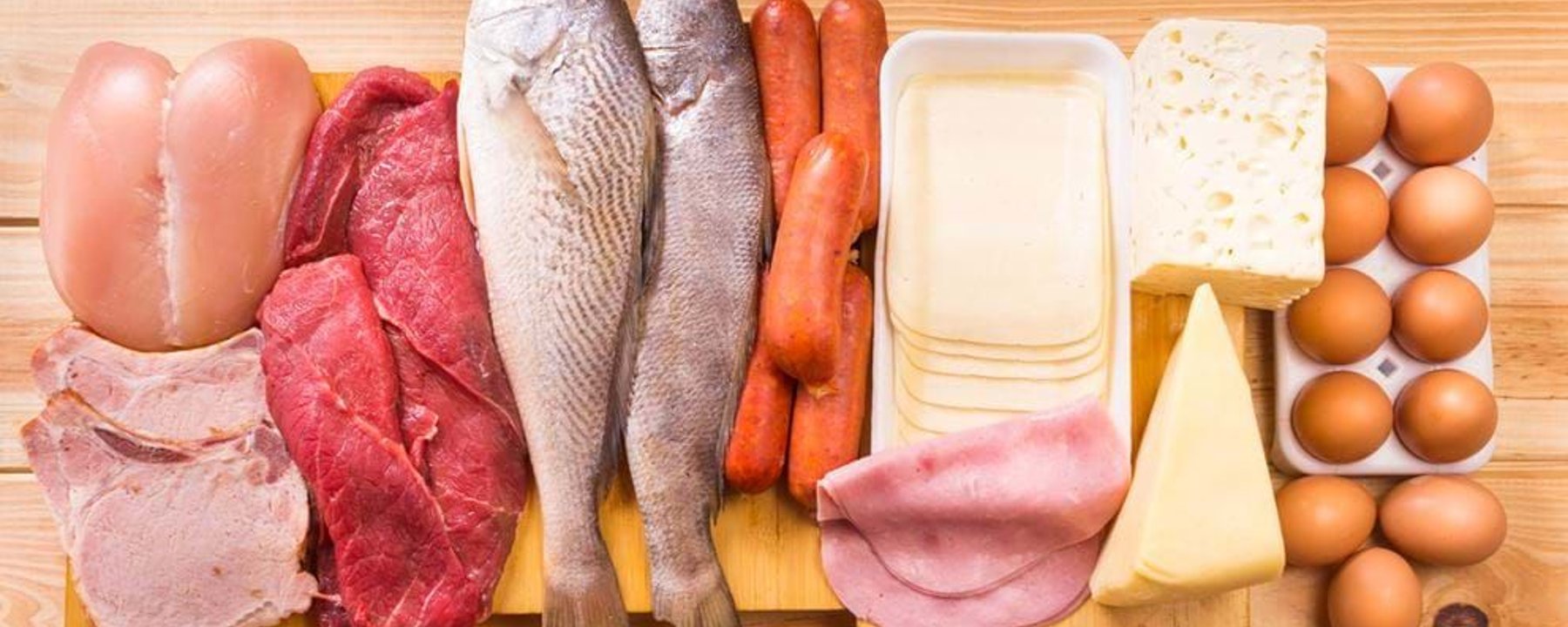Raw chicken, beef, pork, fish, sausages, sliced cheese, ham, cheese blocks, and eggs on wo