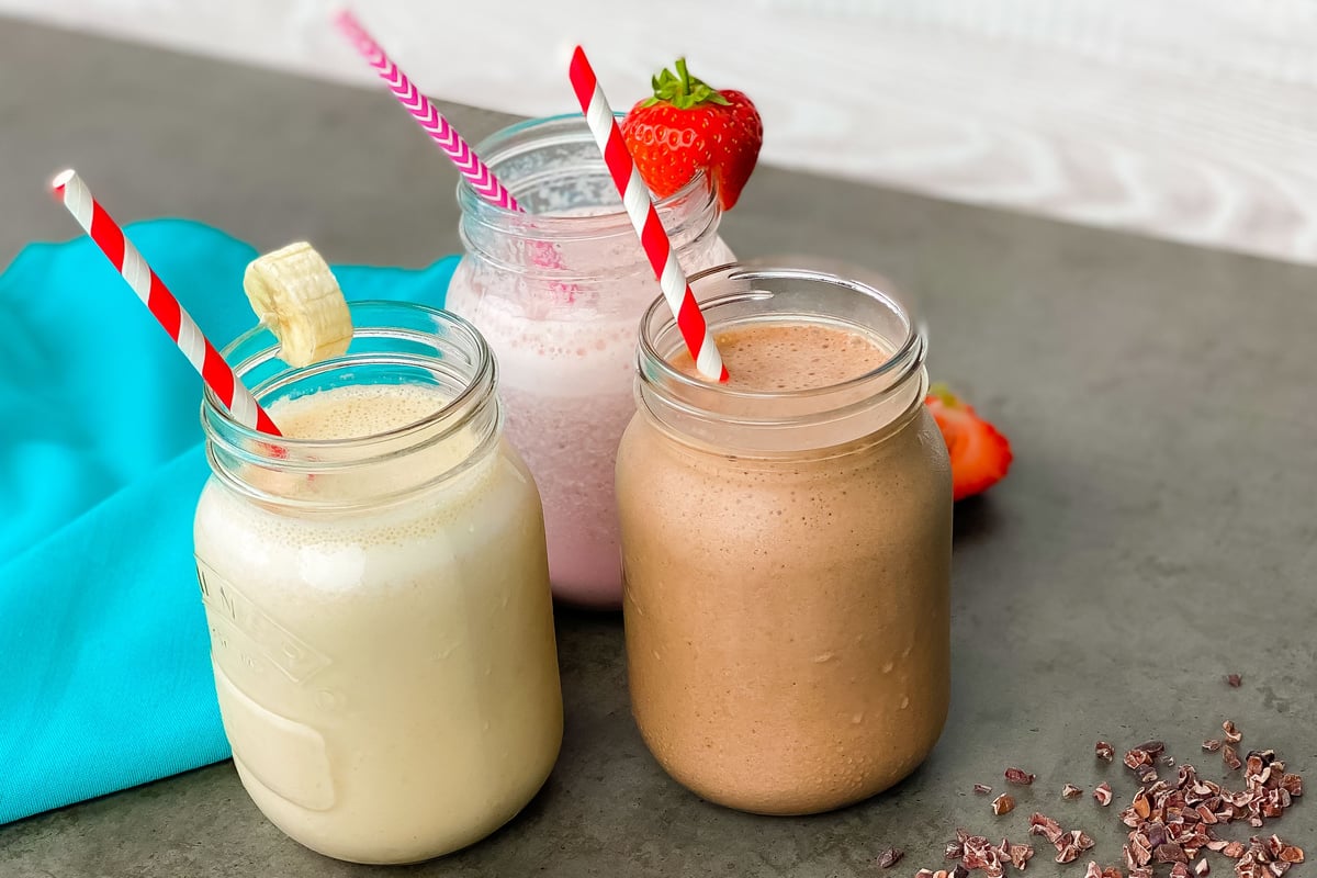 Three protein smoothies in glass jars with striped straws on a grey surface