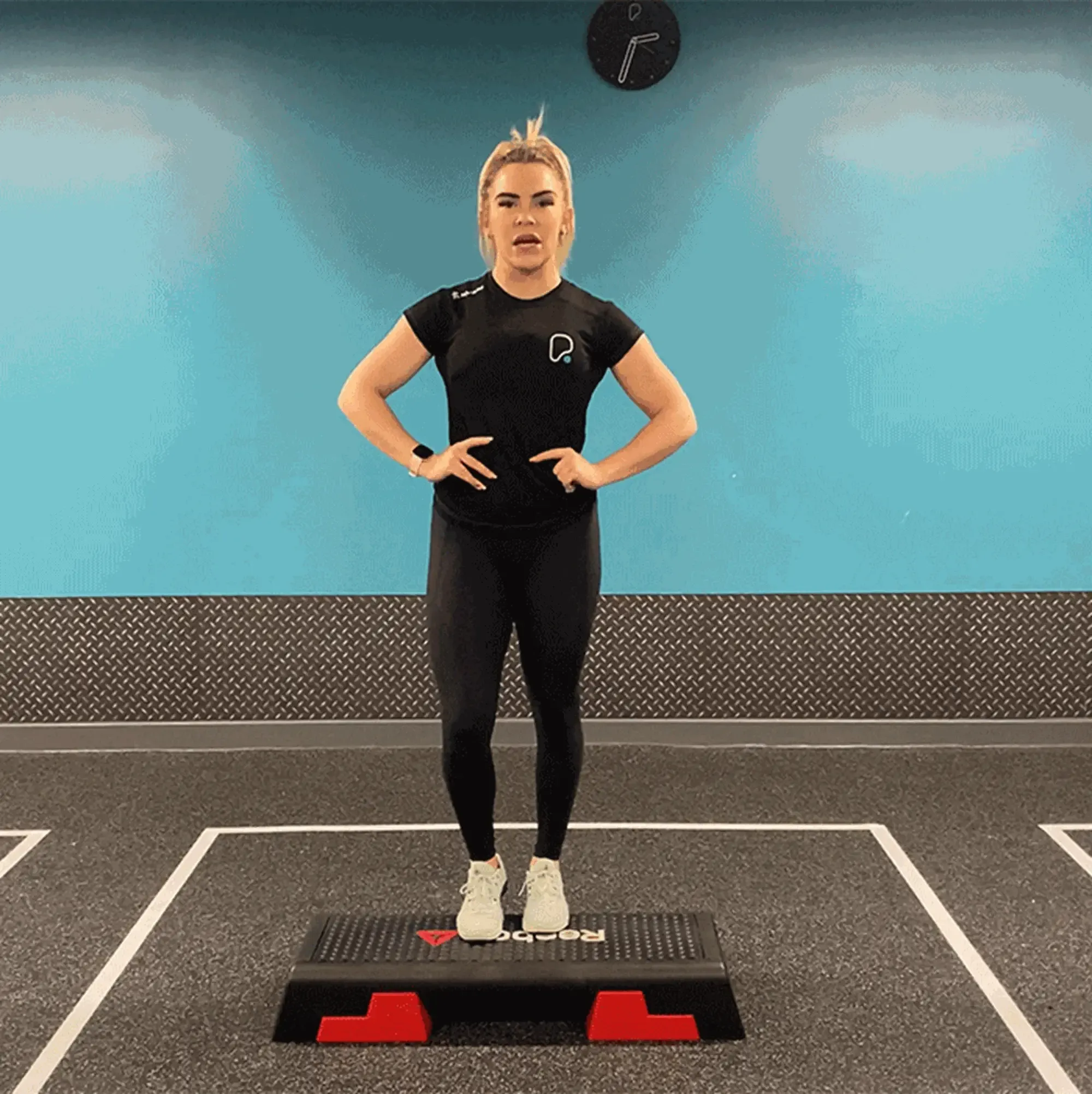 Woman in black sportswear stepping up on a fitness step platform in a gym