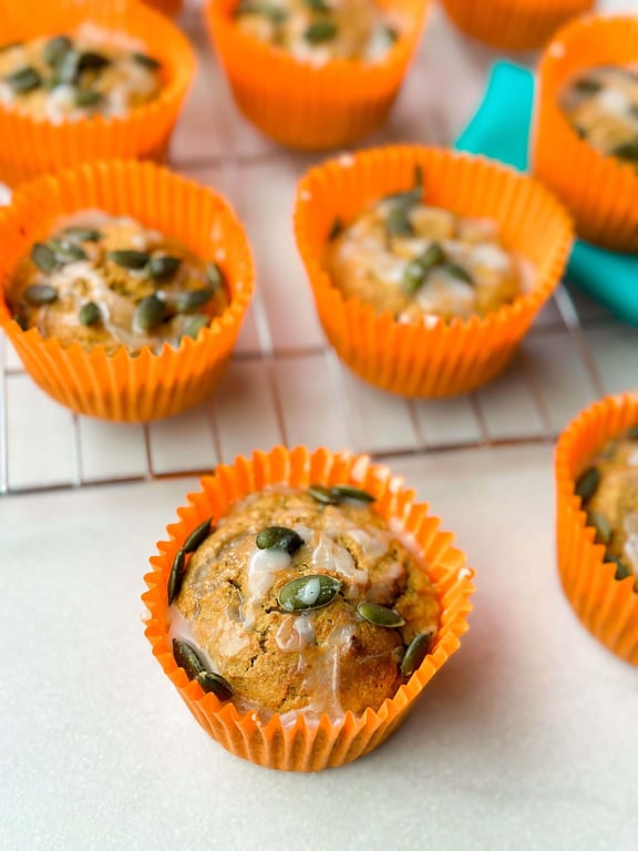 Pumpkin muffins with glaze and pumpkin seeds in orange paper cases on a cooling rack.