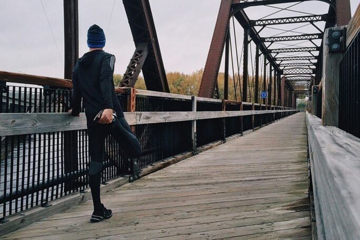 Person dehnt Bein auf Holzbrücke mit Metallträgern an bewölktem Tag