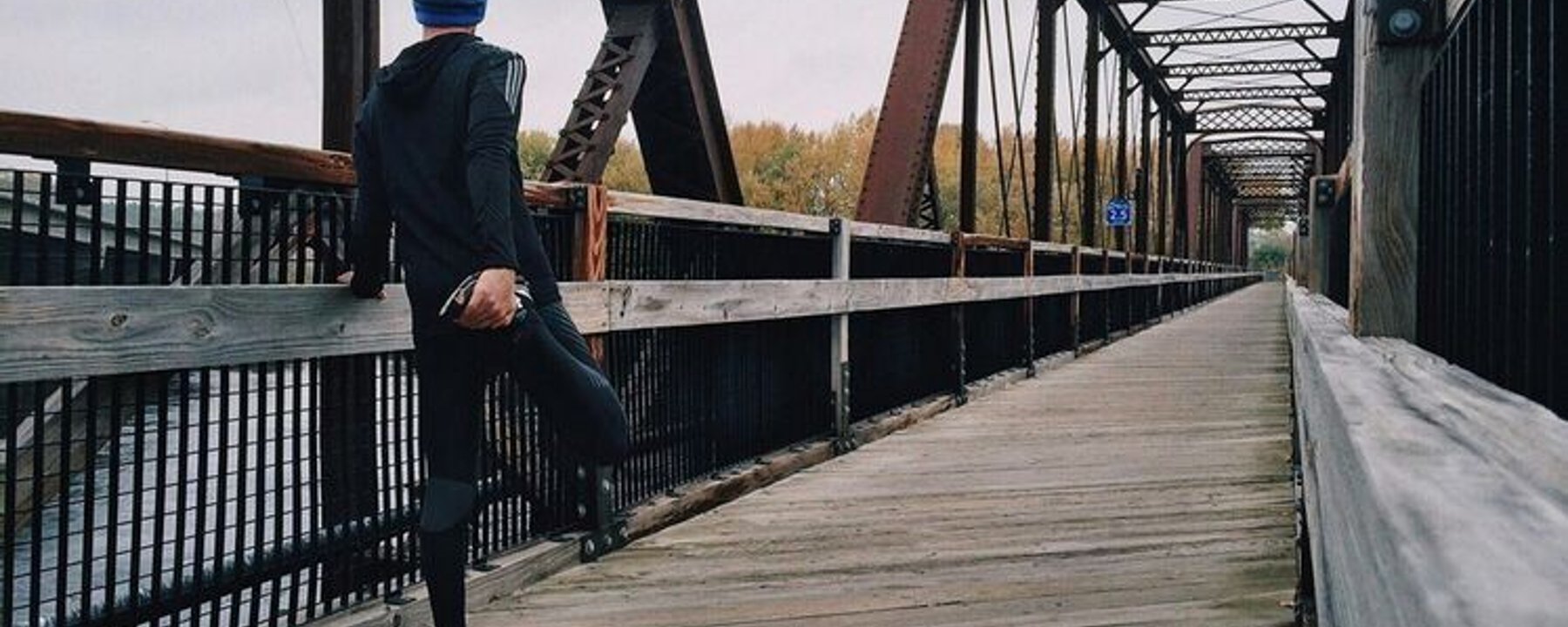 Personne étirant la jambe sur un pont en bois avec poutres métalliques par temps nuageux