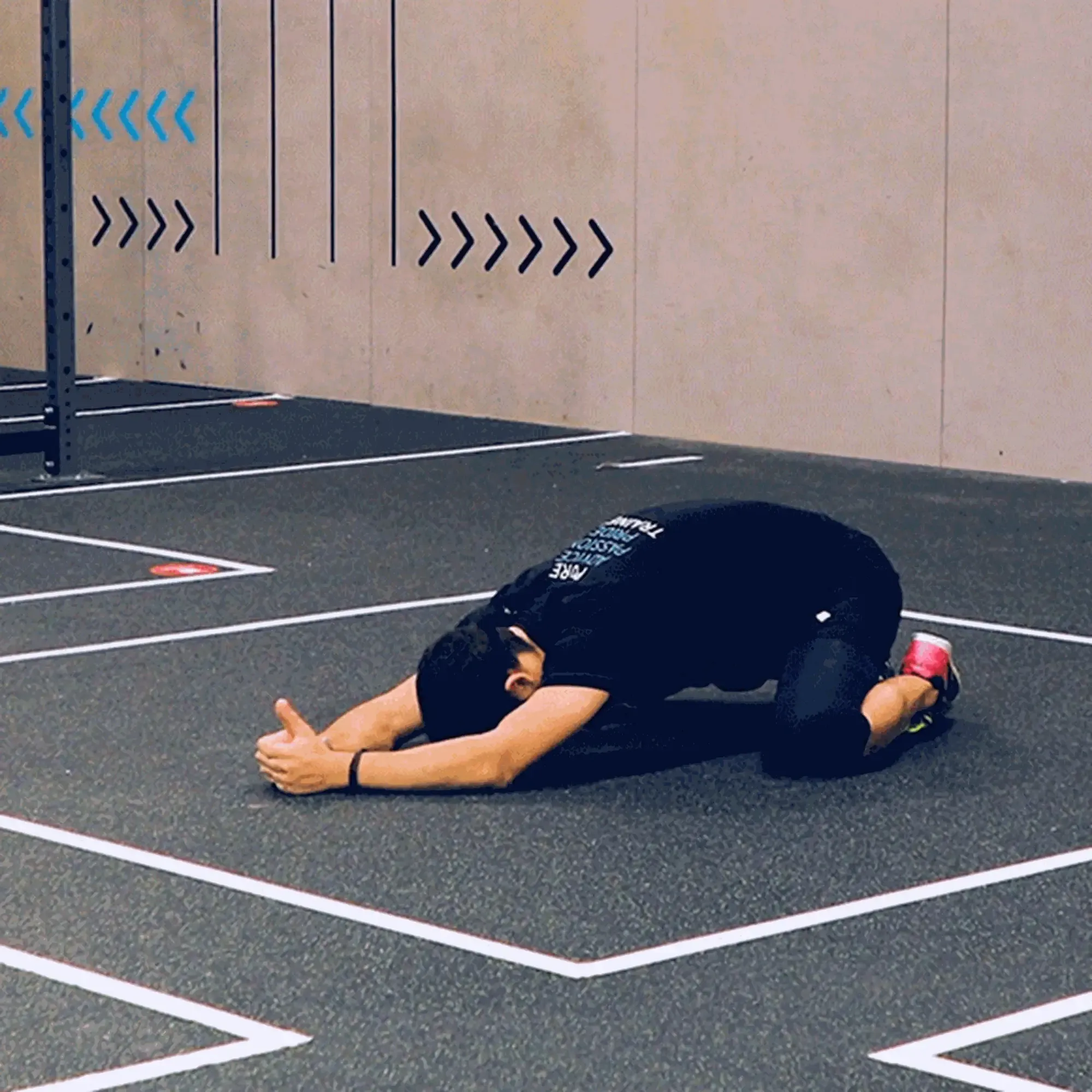 Person stretching on knees with arms extended forward on gym floor marked with white lines