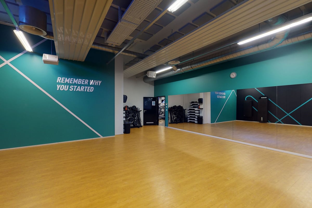 PureGym Chur: Studio mit Spiegelwand, Holzböden und Wänden mit blaugrünen Akzenten.