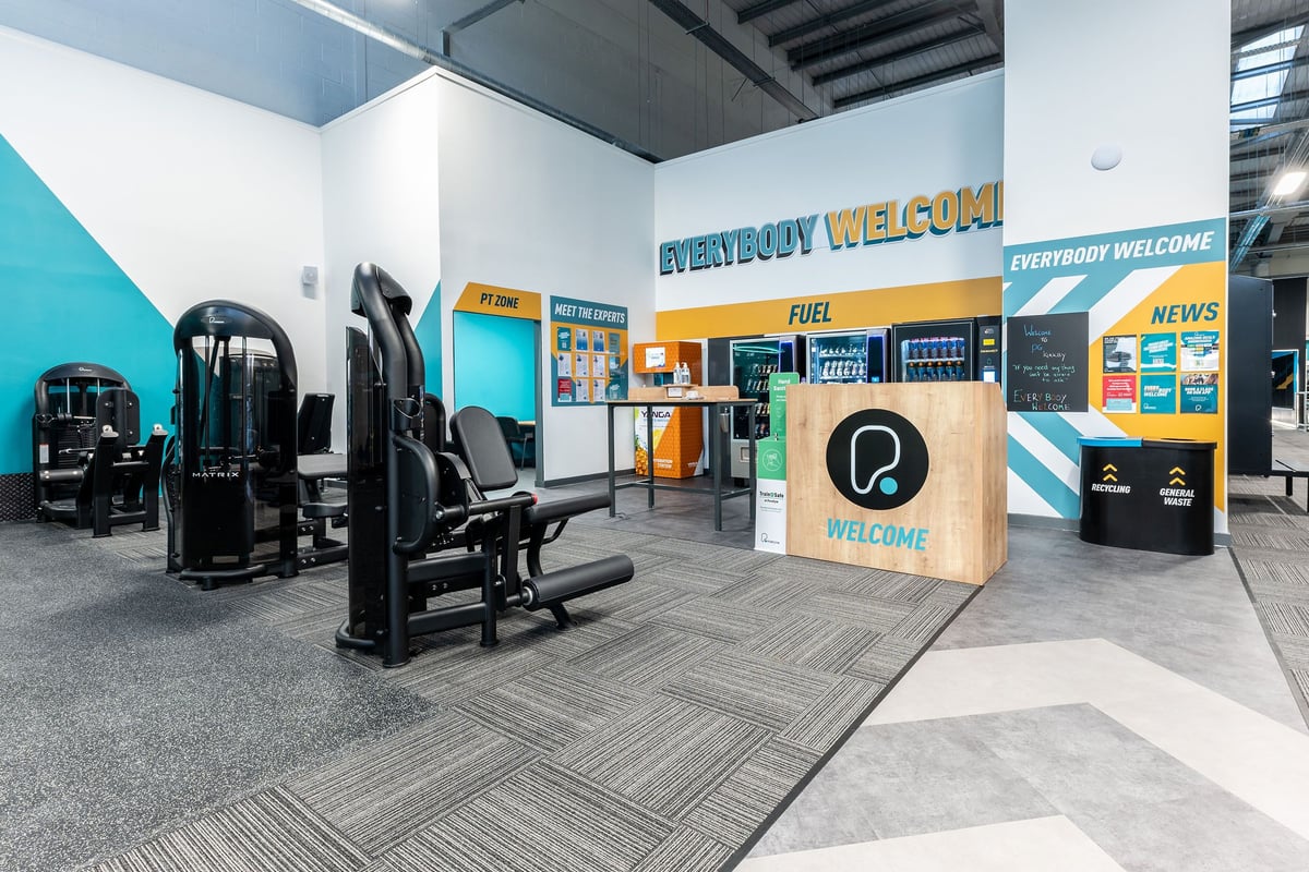 PureGym Kirkby: Resistance machines, cushioned seating, rubberised flooring in a brightly coloured fitness studio.